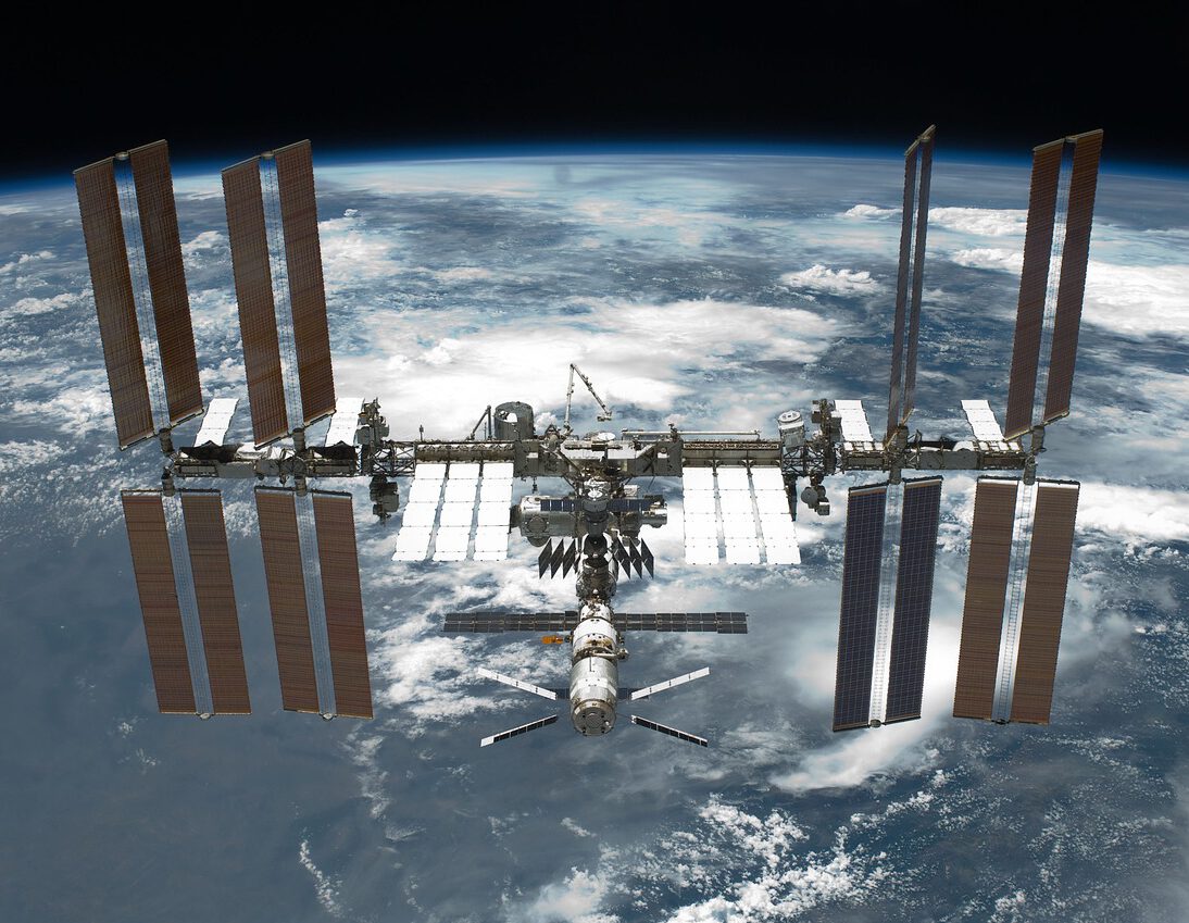 Das Bild zeigt die internationale Raumstation (ISS) die die Erde umkreist. Hinter der ISS ist die Erde zu sehen.